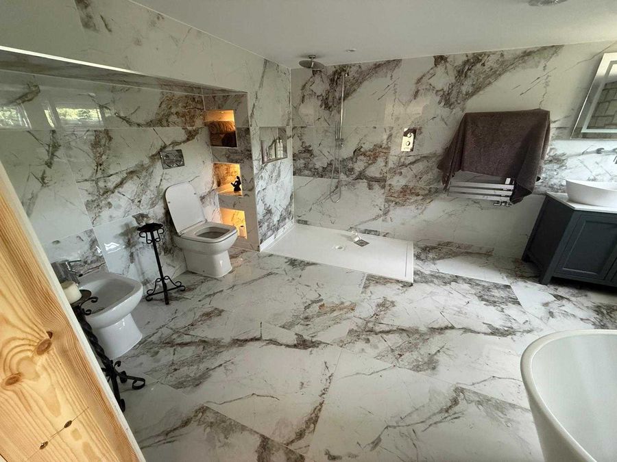 Marble tiled bathroom with a level access walk-in shower and recessed shelving